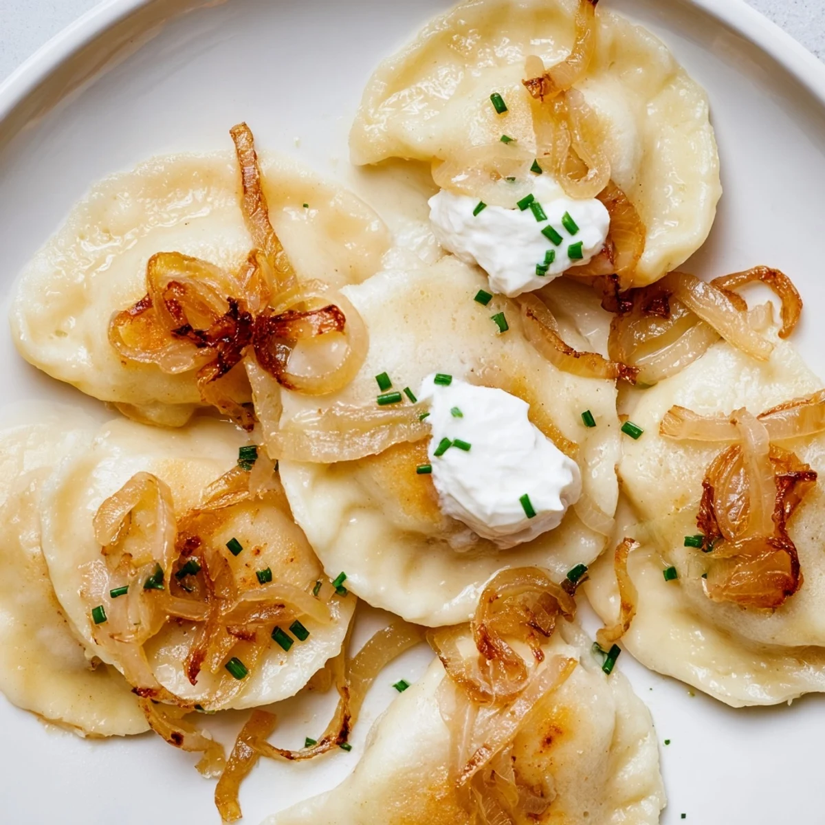 Golden-brown Polish pierogi dumplings, filled with potato and cheese, ready for serving with onions.