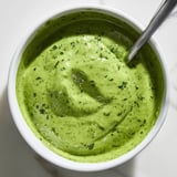 Creamy Green Goddess Dressing in a glass jar with fresh herb garnish and lemon wedges on the side.