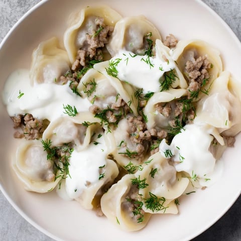 Steaming plate of Russian Pelmeni, richly garnished with creamy sour cream and fresh dill.