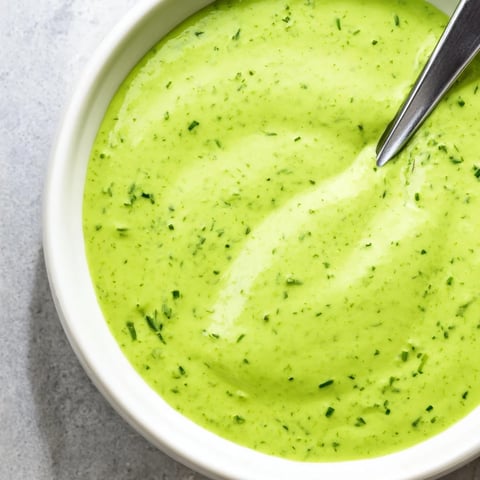 Bright green Green Goddess Dressing drizzled over a fresh salad bowl with avocado slices and cherry tomatoes.