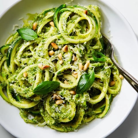 Bright green zucchini noodles sautéed and tossed with a fresh cherry tomato and basil sauce, served in a white bowl.  