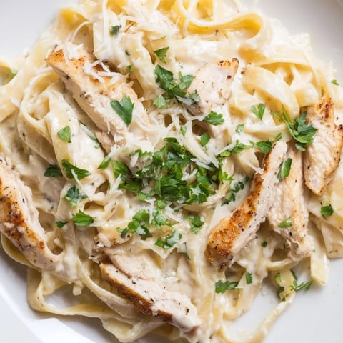 Golden-brown Cajun chicken slices rest atop a creamy white fettuccine Alfredo, garnished with fresh parsley and extra Parmesan.