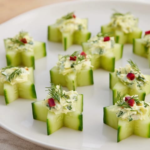Festive Cucumber and Dill Christmas Stars: creamy cheese stars atop cucumber slices, ready to serve as appetizers.