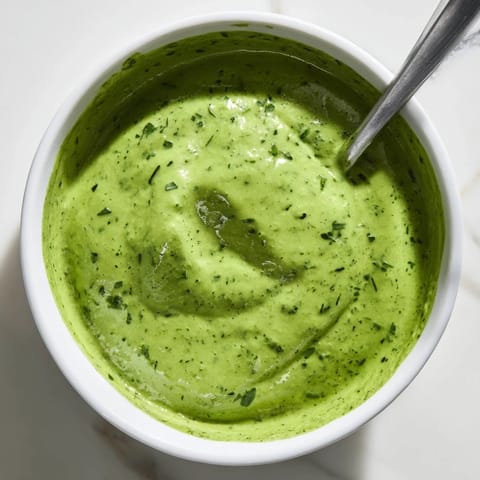 Creamy Green Goddess Dressing in a glass jar with fresh herb garnish and lemon wedges on the side.