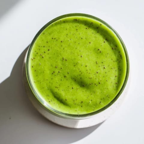 A tall glass of vibrant green spinach-hidden smoothie topped with a fresh mint leaf, perfectly blended and refreshing.  