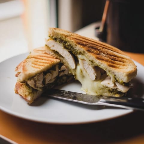 Toasted chicken pesto panini layered with fresh mozzarella and tomato slices on rustic bread.