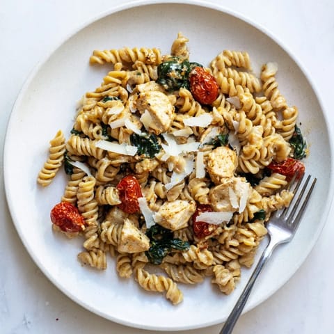 Steam rises from a serving of Greek Yogurt Chicken Pasta, garnished with fresh basil and extra Parmesan, ready for a comforting meal.