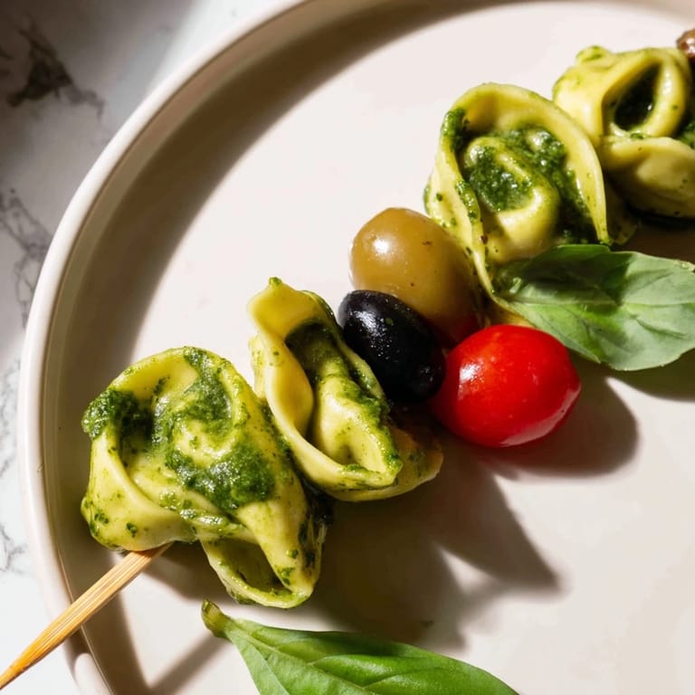 A close-up shot of appetizing Appetizer Skewers, showcasing tortellini, fresh basil, and glossy pesto drizzle.