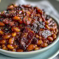 A skillet of savory baked beans with crispy bacon, sweet brown sugar, and smoky paprika, bubbling hot from the oven.