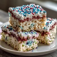 Vibrant red, white, and blue Rice Krispies treats with festive layers and sprinkles for a patriotic dessert.  